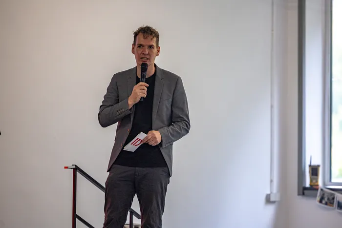 Ein Mann in einem grauen Sakko spricht in ein Mikrofon und hält einen kleinen Zettel in der Hand.