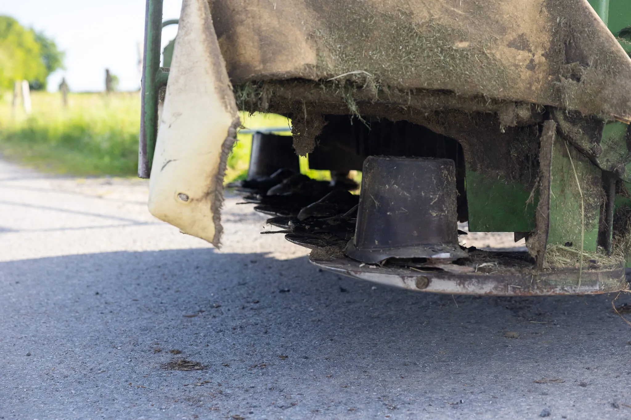 Mähwerk eines landwirtschaftlichen Geräts mit Grasresten über einem Asphaltweg.