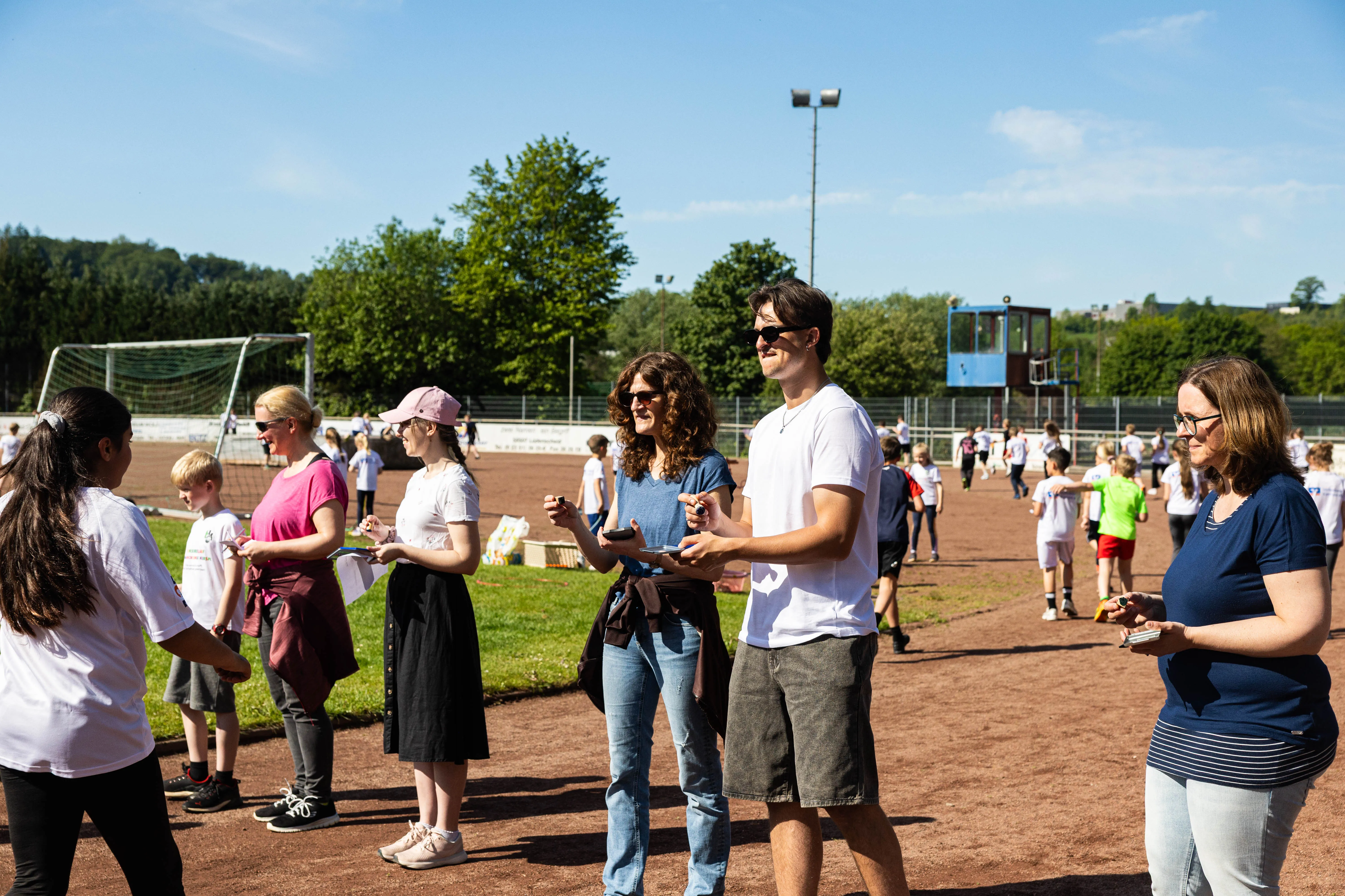 Menschen stehen auf einer roten Aschenbahn und halten Spendenlisten oder Smartphones. Im Hintergrund ein Fußballtor und Bäume.