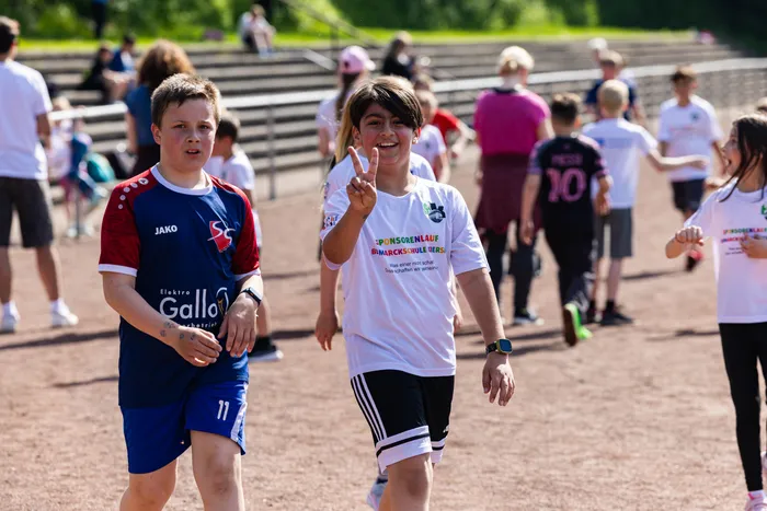 Zwei Schülerinnen und Schüler beim Spendenlauf der Bismarckschule Kierspe, die Schülerin zeigt die Zahl Zwei mit den Fingern.