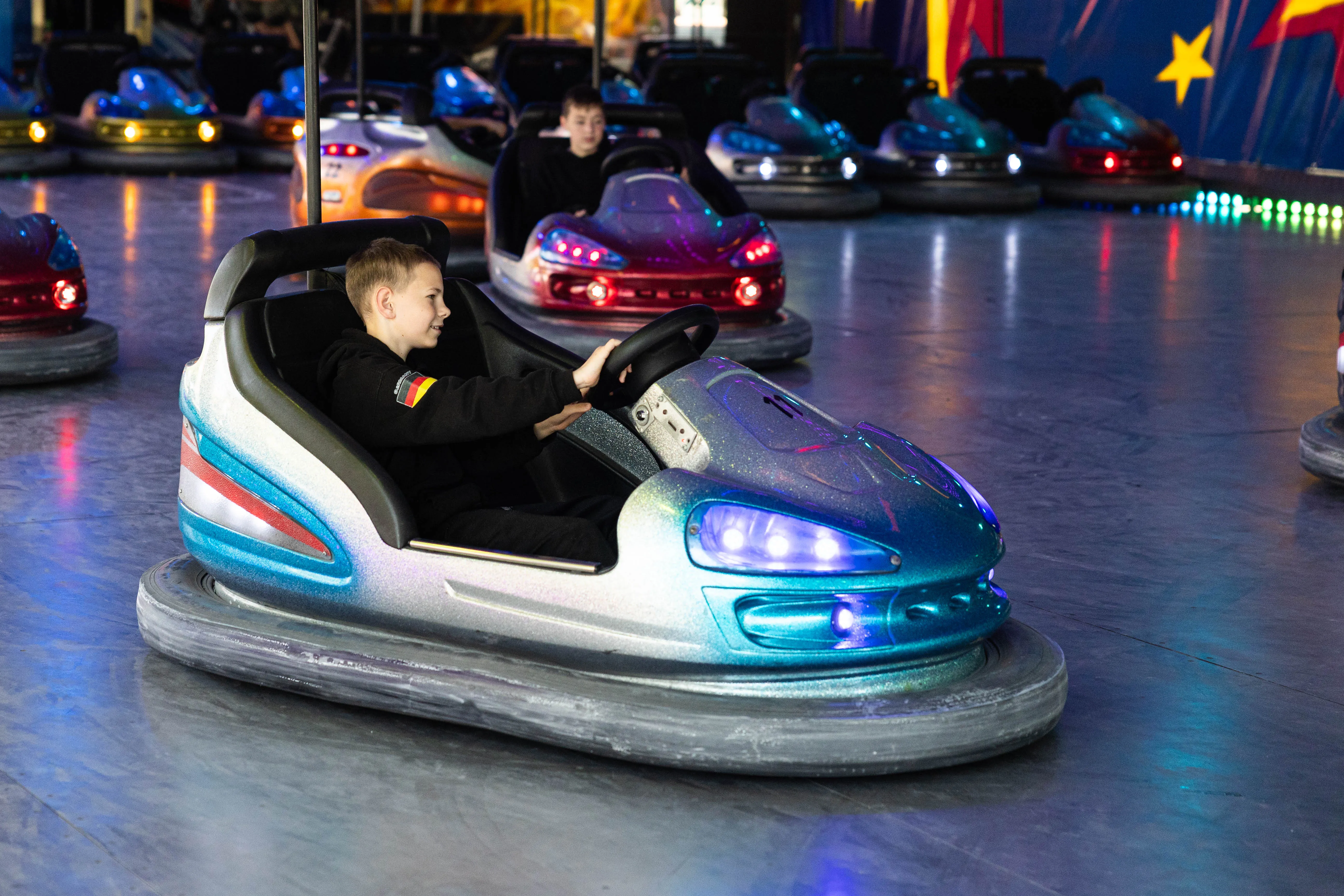 Junge fährt auf der Kirmes ein Elektroauto. Im Hintergrund sind weitere Autos und Besucher zu sehen.