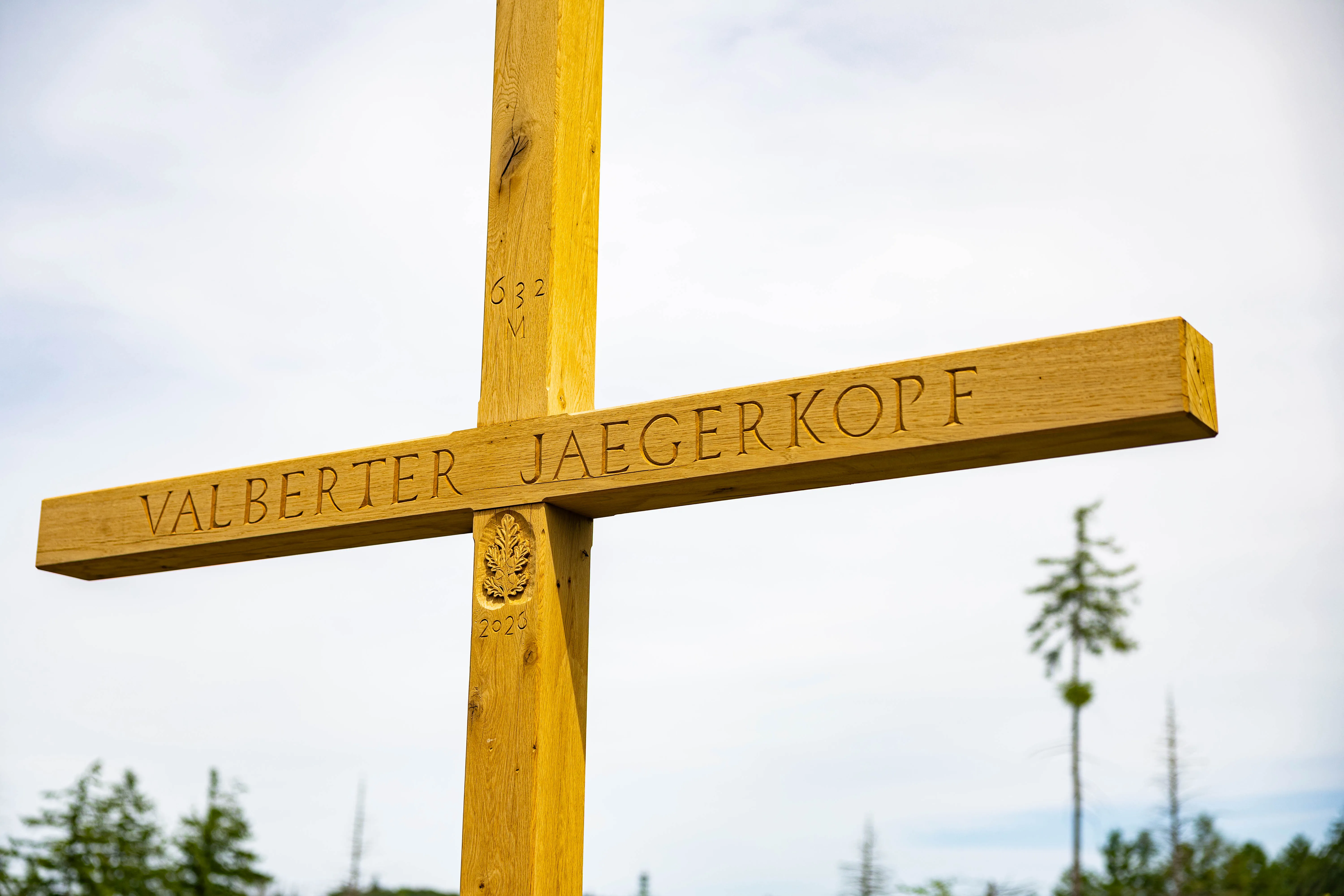 Holzkreuz mit der Inschrift „VALBERTER JAEGERKOPF“ und dem Jahr „2024“ sowie „632 V“ im oberen Teil, vor einem bewaldeten Hügel.