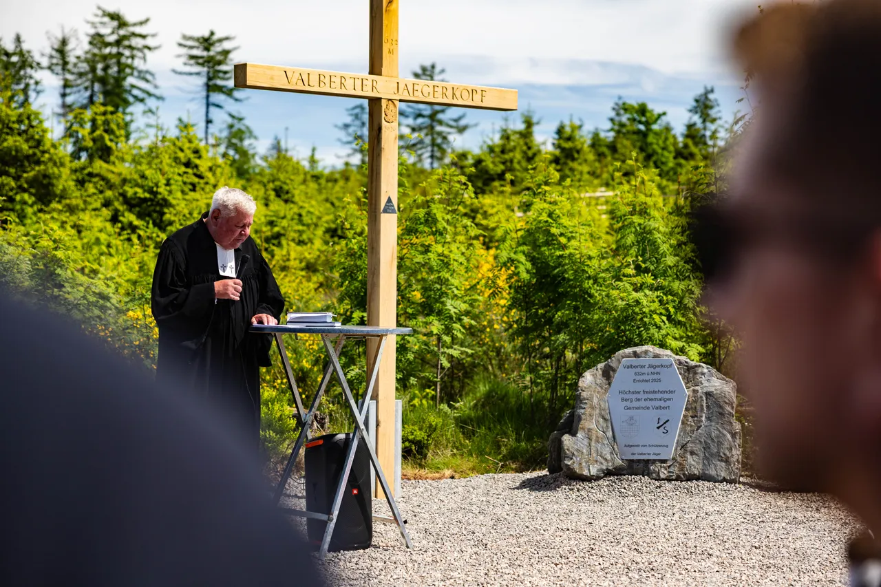 Ein Priester hält während eines Eröffnungsgottesdienstes am Valberter Jägerkopf eine Predigt vor einem Holzkreuz und einer Gedenktafel.