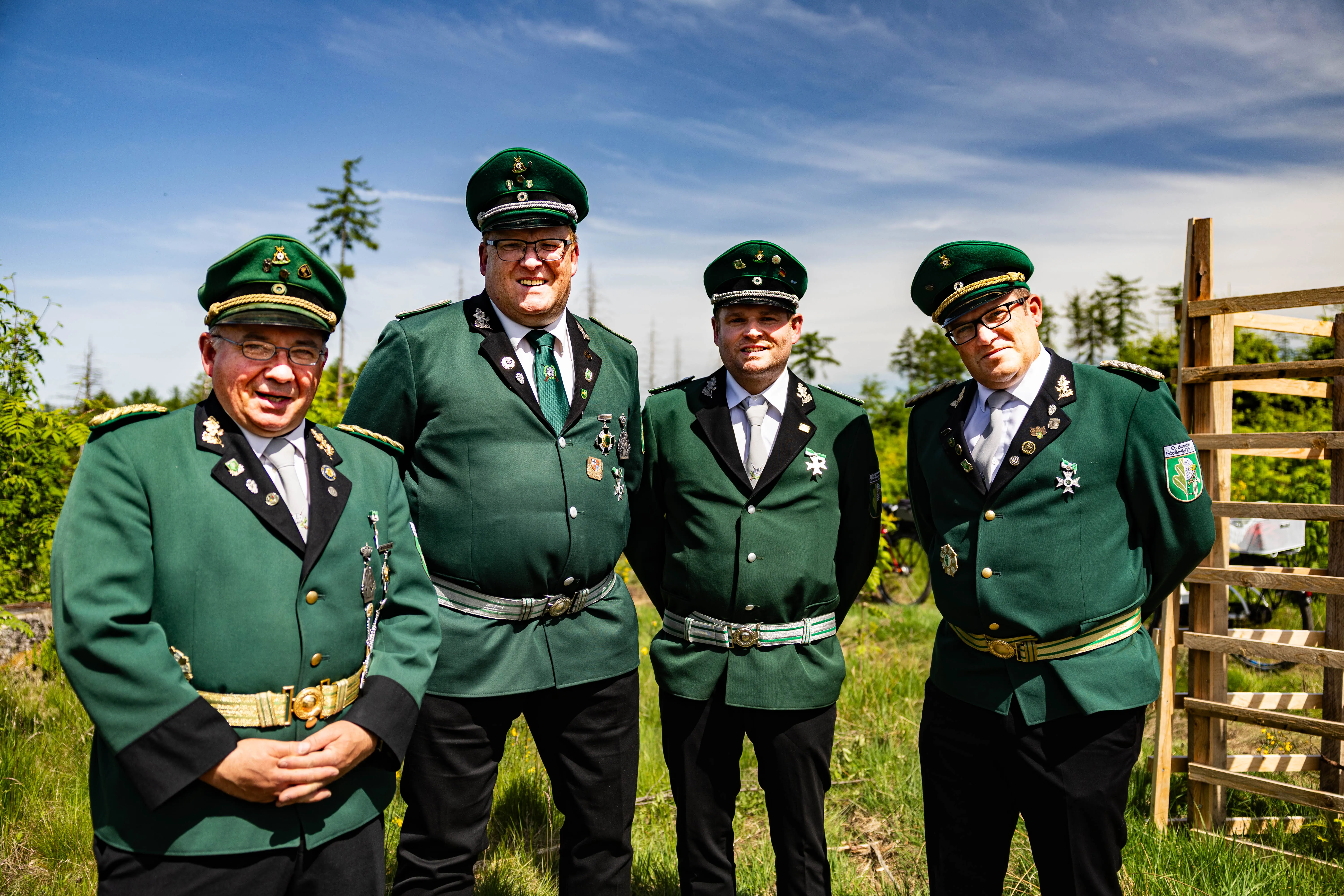 Vier Männer in grünen Jägeruniformen mit zahlreichen Abzeichen und Orden stehen lächelnd nebeneinander im Freien.