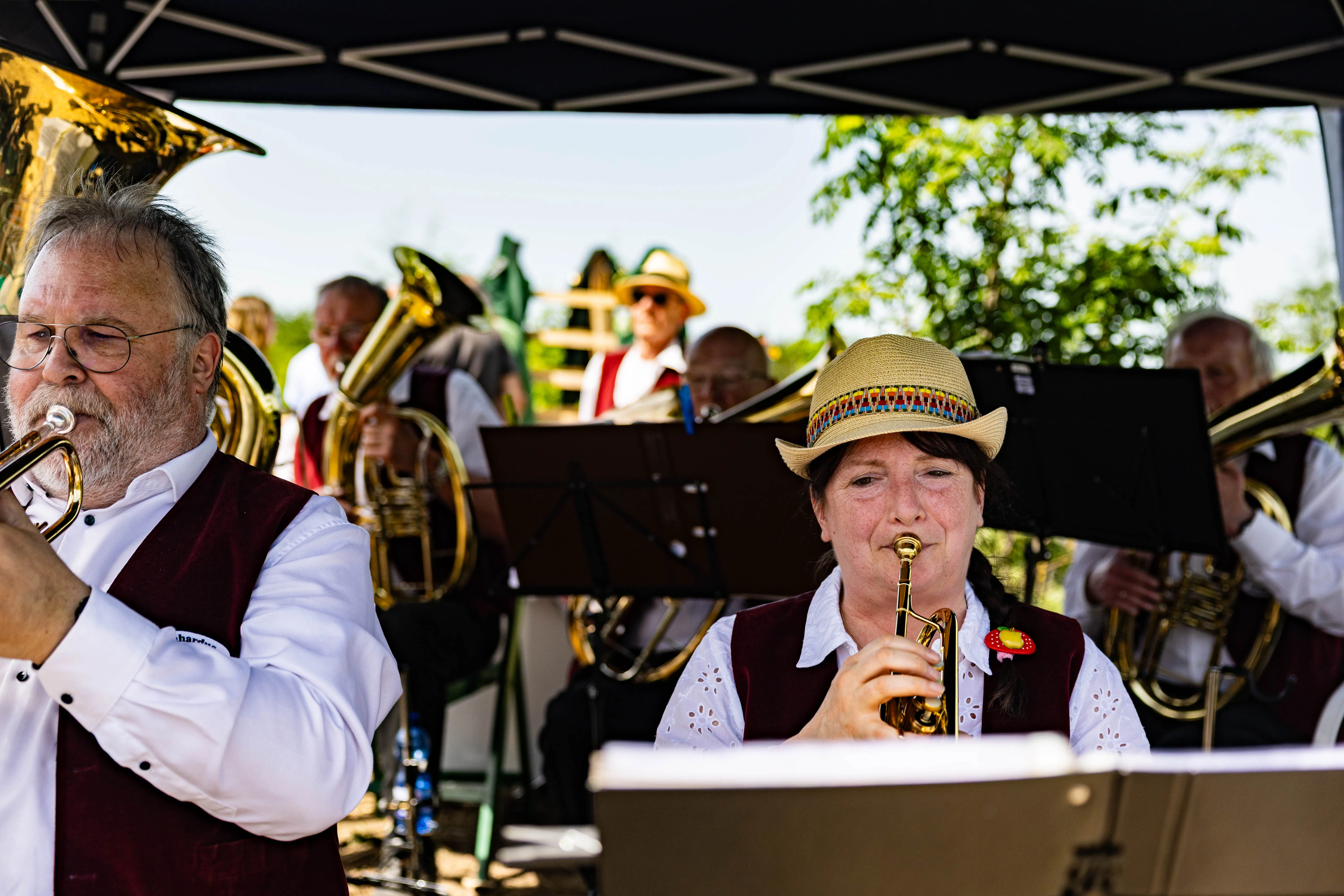 Zwei Musiker spielen Posaune und Trompete während eines Eröffnungsgottesdienstes im Freien. Im Hintergrund weitere Bläser und Zuschauer.