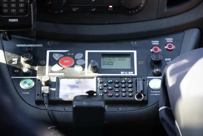 Funkgerät mit Tasten und Display im Cockpit eines Polizeifahrzeugs, daneben ein Funkmikrofon.