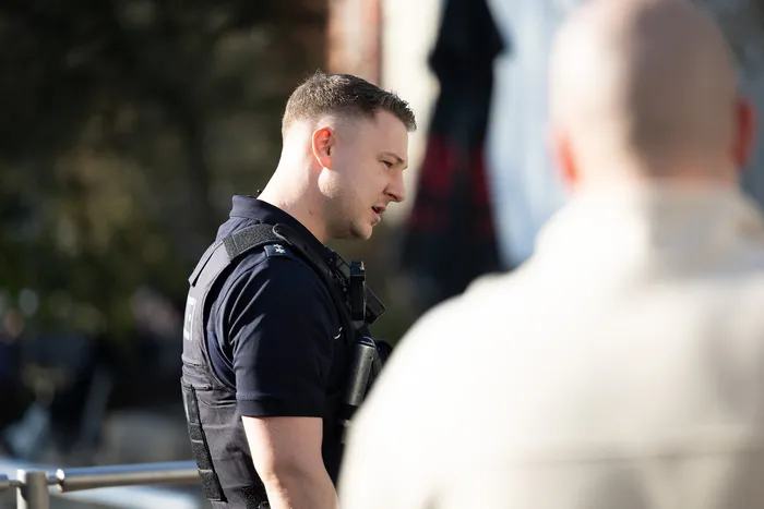 Ein Polizist in Uniform und Schutzweste steht im Dienst und blickt nachdenklich in die Ferne.