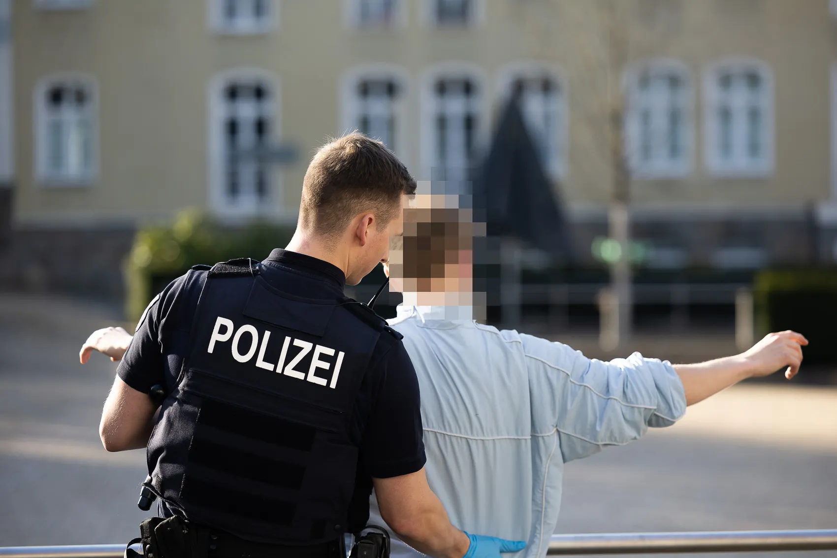 Ein Polizist mit der Aufschrift „POLIZEI“ auf der Weste durchsucht eine Person mit erhobenen Armen.