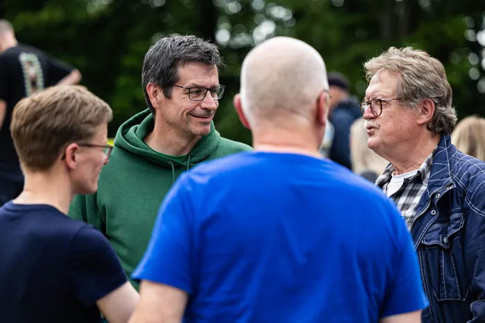 Drei Männer und eine Frau stehen im Gespräch vor grünem Hintergrund. Von links sind Sina Löschke (Grüne), ein Mann mit blauem Hoodie, ein Mann mit Glatze und Jürgen Wichert (SPD) zu erkennen.