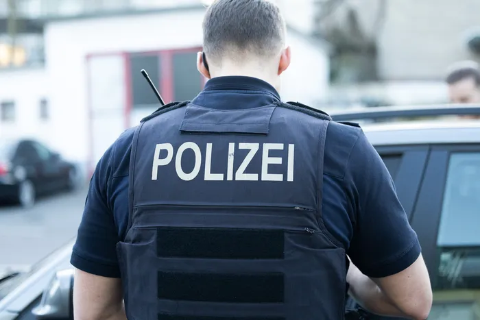 Rückansicht einer Person mit der Aufschrift „POLIZEI“ auf der Schutzweste, vermutlich ein Polizist im Einsatz.