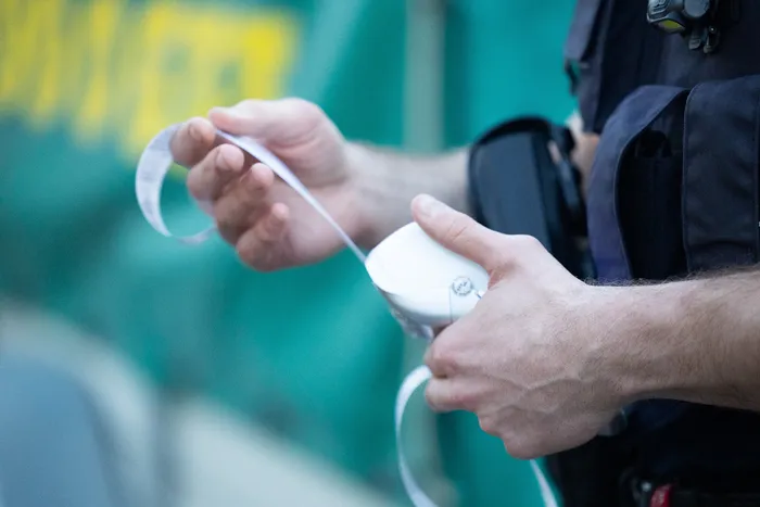 Ein Polizist hält ein weißes Gerät in der Hand und führt eine Messung durch, während er einen weißen Streifen hält.