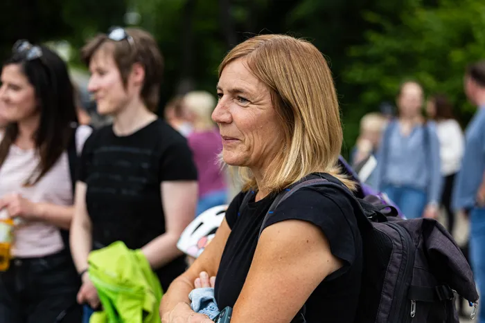 Eine Frau mit blonden Haaren und einem Rucksack blickt zur Seite, während im Hintergrund weitere Menschen stehen. Sie ist Regionalmanagerin Susanne Neumann bei der Eröffnung des Skateparks in Halver.