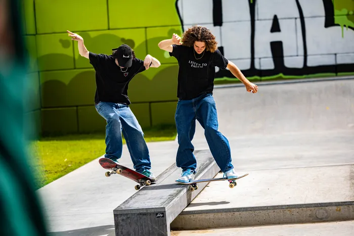 Zwei junge Männer fahren auf Skateboarden über eine Betonkante im neu eröffneten Skatepark in Halver. Im Hintergrund ist ein Graffiti-Wand zu sehen.