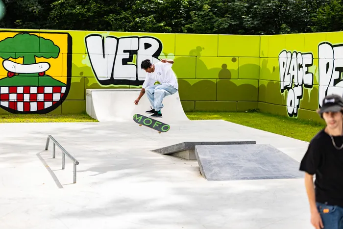 Ein Skater fährt auf einem grünen Skateboard über eine Rampe im neu eröffneten Skatepark in Halver. Im Hintergrund ist ein farbenfrohes Wandgemälde mit dem Schriftzug „VER“ und einem Wappen zu sehen.