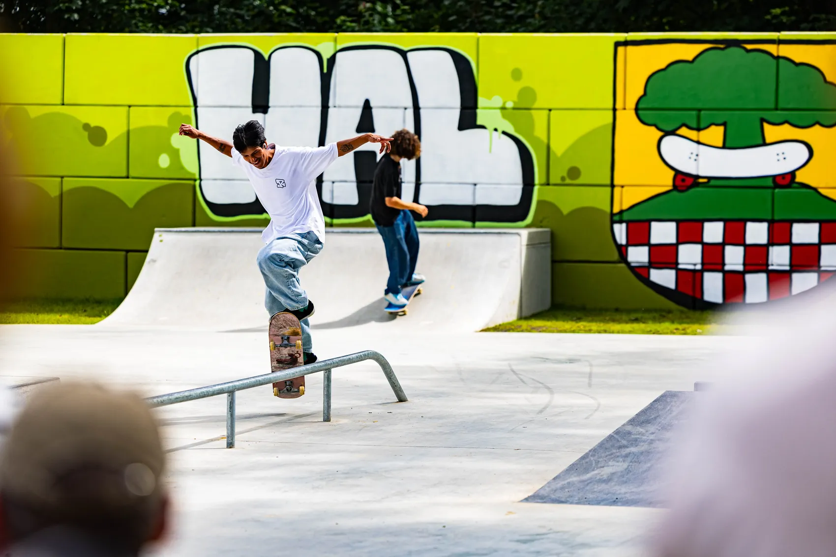 Ein Skater balanciert auf einem Geländer in der neu eröffneten Skateranlage in Halver, während ein zweiter Skater im Hintergrund fährt. Im Hintergrund ist eine bunt bemalte Wand zu sehen.