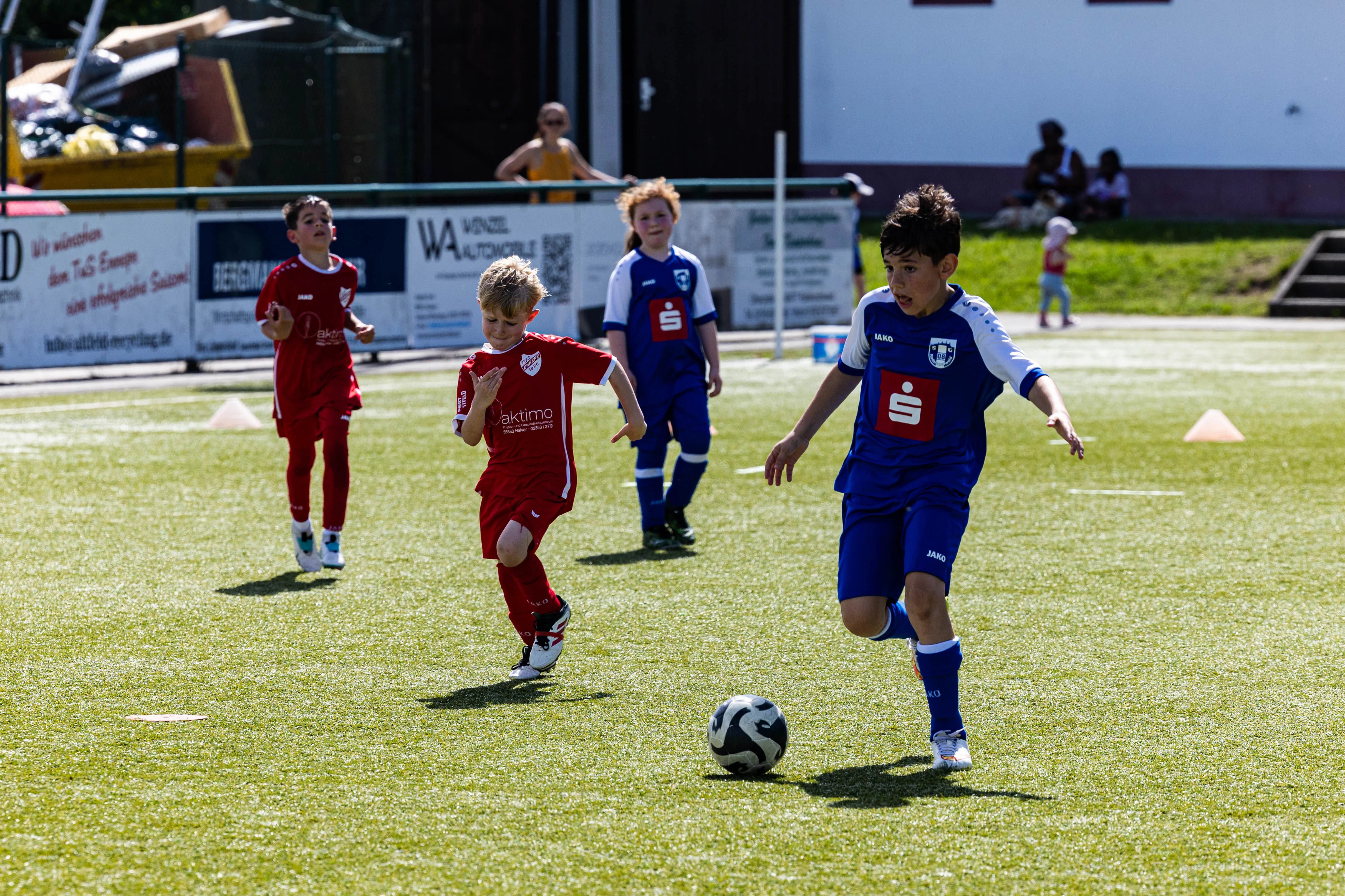Junge Fußballspieler in roten und blauen Trikots während eines Turniers auf einem Rasenplatz.