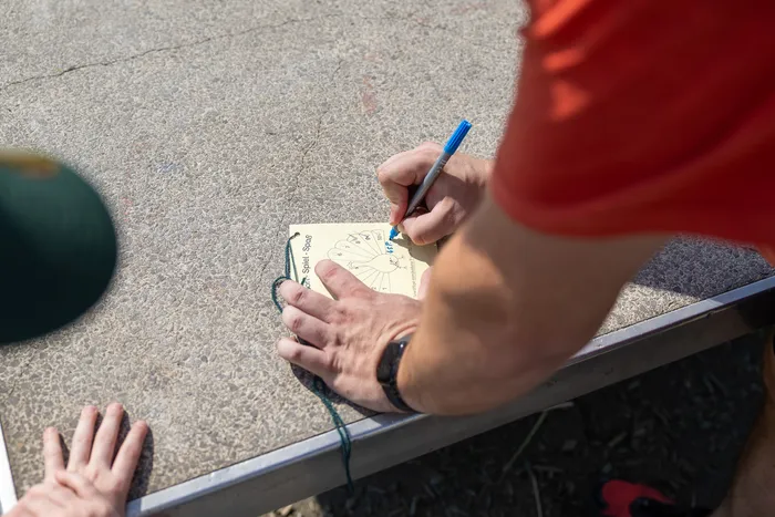 Eine Person markiert auf einer farbigen Karte mit einem blauen Stift, während sie einen Seilabschnitt hält. Im Hintergrund ist eine weitere Person in roter Kleidung zu sehen.