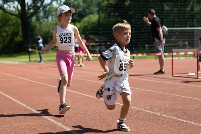 Zwei Kinder laufen auf einer roten Tartanbahn bei einem Wettkampf. Das Mädchen trägt eine Startnummer 923, der Junge 85.