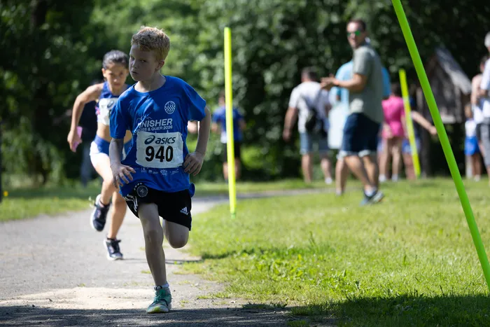 Ein Junge mit rotem Haar läuft bei dem Cross und Quer Wettbewerb 2026 auf einem Waldweg. Im Hintergrund sind weitere Läufer und Zuschauer zu sehen.