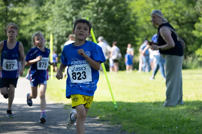 Ein Junge mit der Startnummer 823 rennt bei einem Crosslauf voran, während andere Läufer und Zuschauer im Hintergrund zu sehen sind.