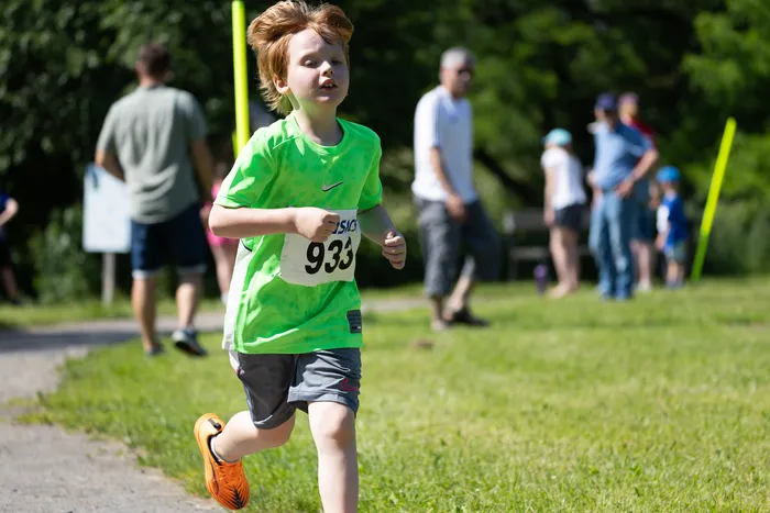 Ein rothaariger Junge mit der Startnummer 933 rennt bei einem Crosslauf. Im Hintergrund sind weitere Läufer und Zuschauer zu sehen.