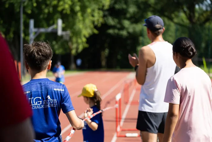 Ein Junge mit blauem Trikot des Vereins „TG Halver“ geht auf einer roten Laufbahn einem Hindernis entgegen, während im Hintergrund Zuschauer applaudieren.