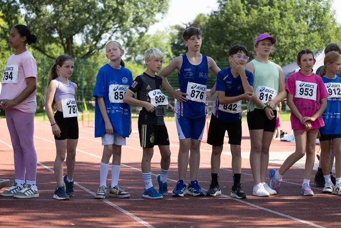 Eine Gruppe von Kindern und Jugendlichen steht auf einer Laufbahn bereit für den Start eines Wettlaufs. Sie tragen Sportkleidung und Startnummern.