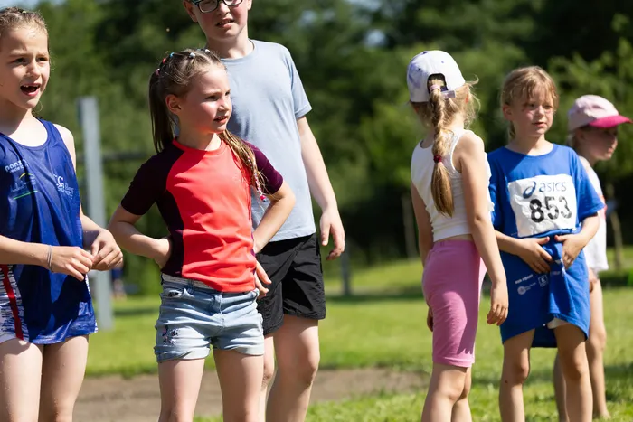Eine Gruppe von Kindern und Jugendlichen steht auf einer Wiese, einige tragen Sportkleidung und Startnummern. Sie scheinen sich auf einen Lauf vorzubereiten.