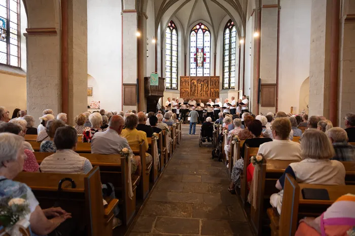 Ein Chor singt in einer Kirche vor einer versammelten Gemeinde. Die Kirchenbänke sind gefüllt mit Menschen unterschiedlichen Alters.