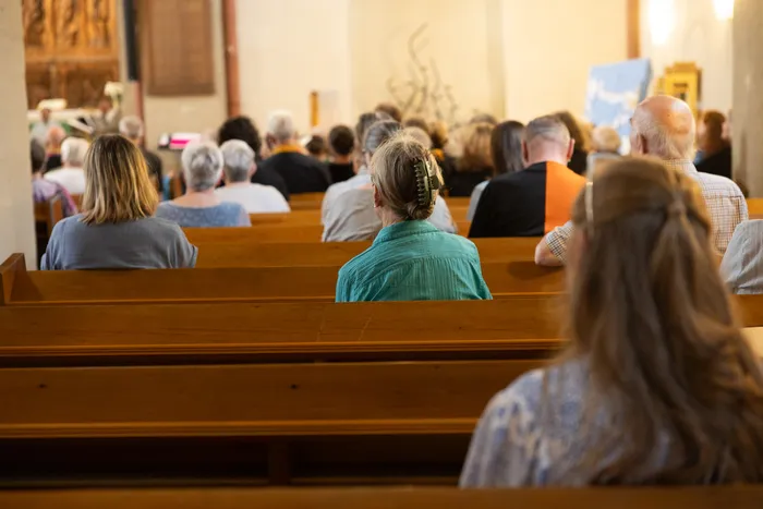 Menschen sitzen auf Holzbänken in einer Kirche, dem Chor zugewandt. Das Bild zeigt die Gemeinde während eines Konzerts in der Jakobus-Kirche.
