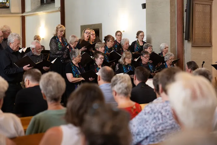 Ein Chor singt in einer hellen Kirche, während im Publikum viele Menschen sitzen und zuhören.