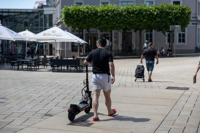 Ein Mann fährt mit einem E-Scooter auf einem gepflasterten Platz, während im Hintergrund Passanten und Cafés zu sehen sind. Die Aufnahme entstand im Rahmen von Polizeikontrollen zur Einhaltung der Verkehrsregeln in der Fußgängerzone.