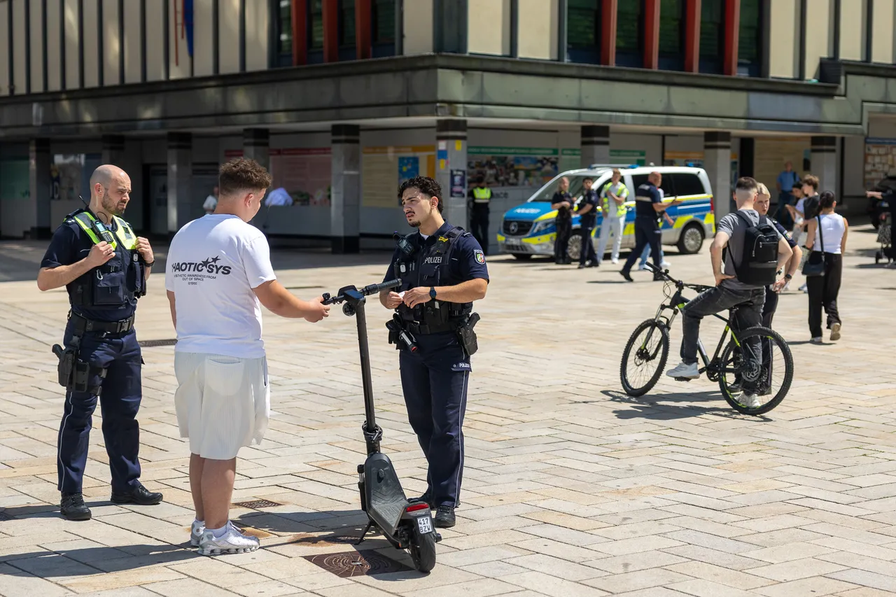 Polizisten kontrollieren einen jungen Mann auf einem E-Scooter in einer Fußgängerzone. Im Hintergrund sind weitere Beamte und Passanten zu sehen.
