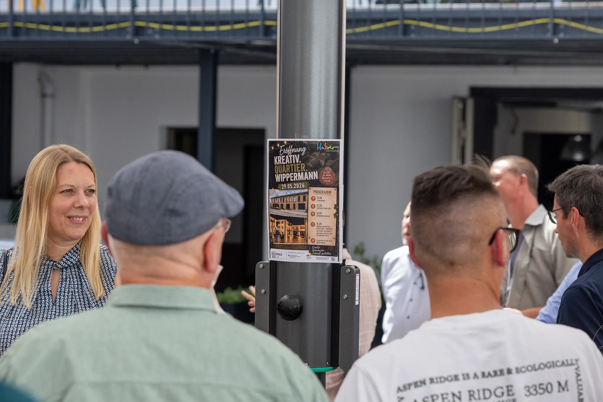 Menschengruppe betrachtet Plakat zur Eröffnung des Kreativ.Quartier.Wippermann am 25.05.2026.