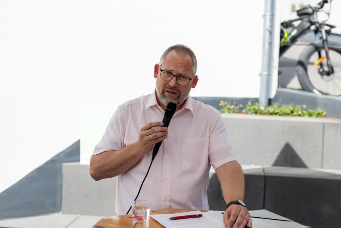Mann mit Brille hält Rede vor Publikum, Notizen liegen auf dem Tisch vor ihm.