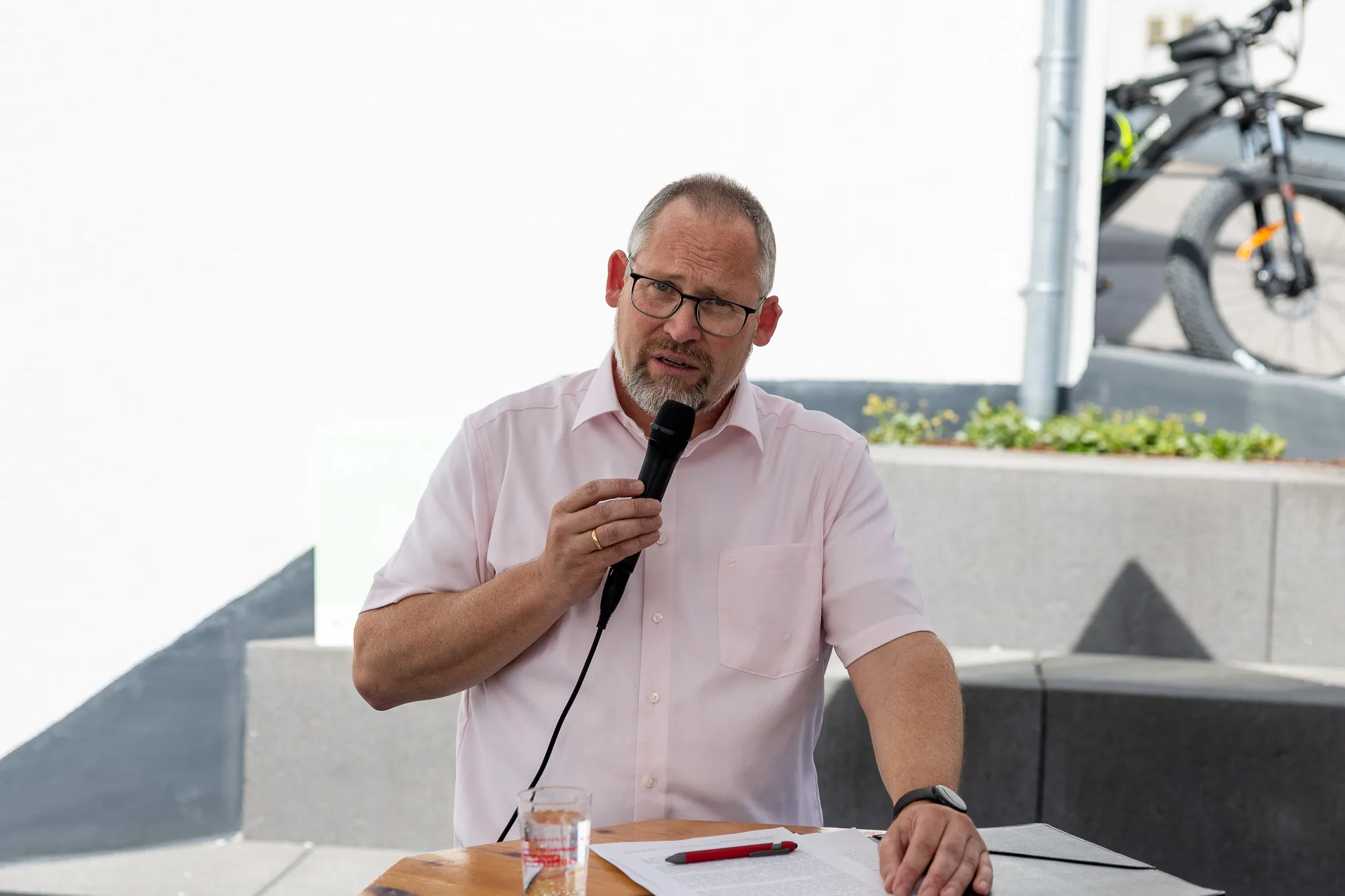 Mann mit Brille hält Rede vor Publikum, Notizen liegen auf dem Tisch vor ihm.