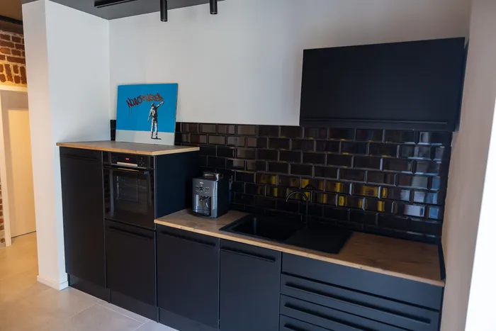 Moderne Küche mit schwarzen Schränken und einer Arbeitsplatte aus hellem Holz. Über dem Backofen hängt ein farbenfrohes Kunstwerk.