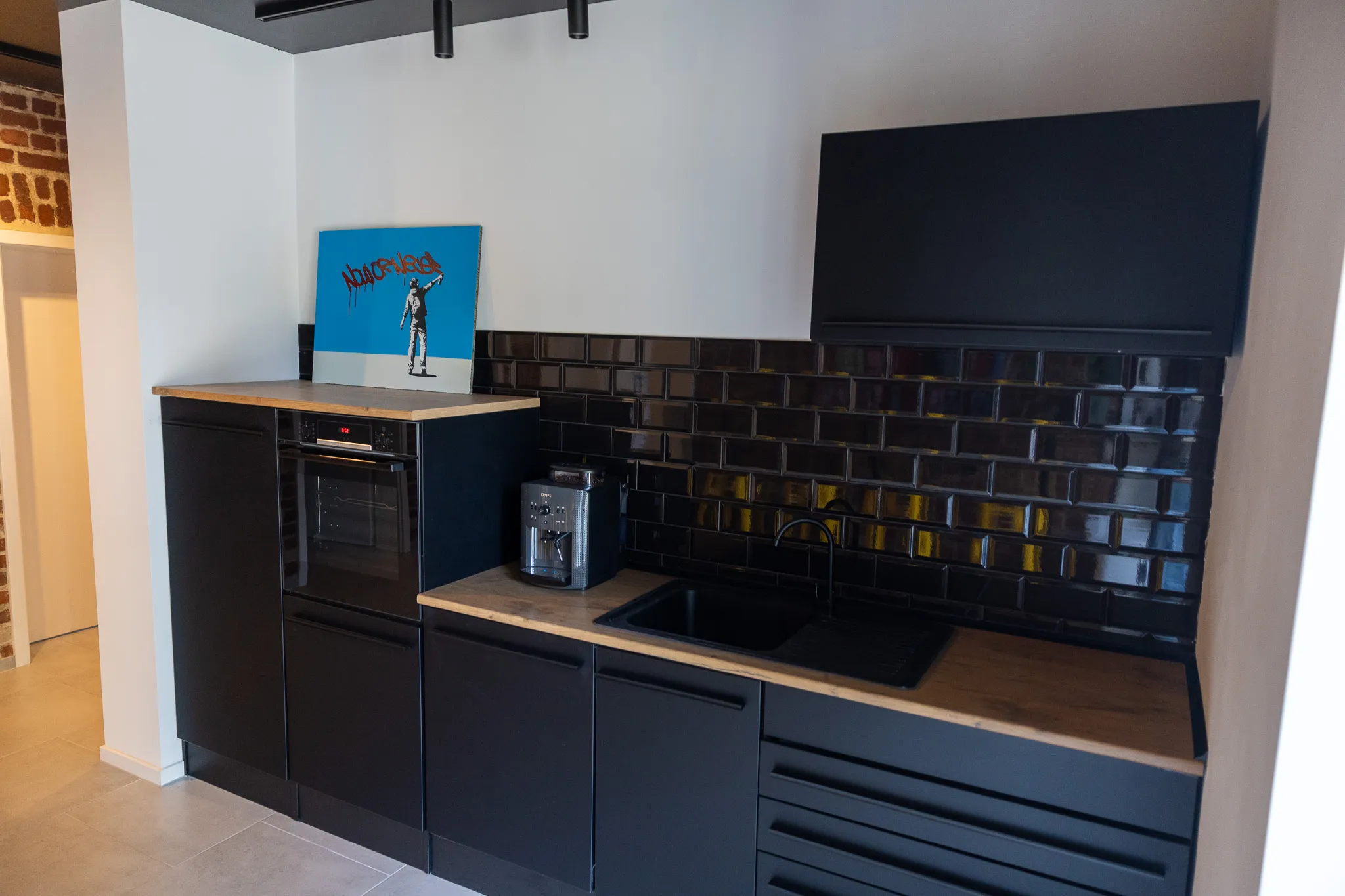 Moderne Küche mit schwarzen Schränken und einer Arbeitsplatte aus hellem Holz. Über dem Backofen hängt ein farbenfrohes Kunstwerk.