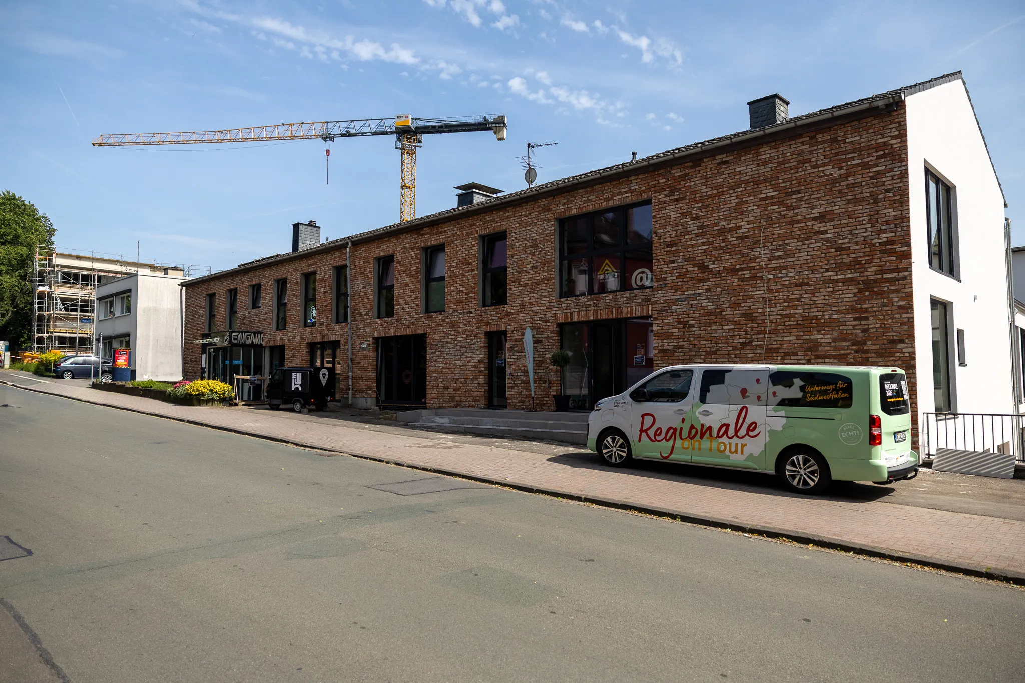 Zweistöckiges Backsteingebäude mit großen Fenstern, davor ein Lieferwagen mit der Aufschrift „Regionale on Tour“ und im Hintergrund ein Baugerüst mit Kran.