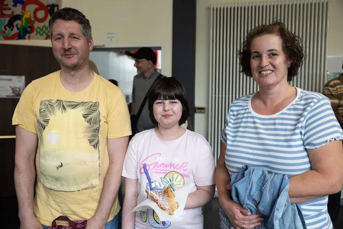 Vater, Tochter und Mutter stehen lächelnd vor der Kamera. Die Tochter hält einen frisch gebackenen Pfannkuchen in der Hand.