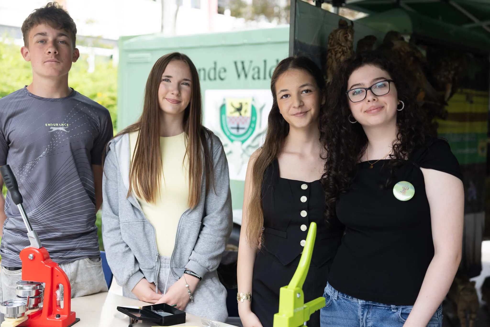 Vier Jugendliche stehen vor einem Fahrzeug mit dem Aufdruck „Freunde Wald“. Sie halten Modelle und Werkzeuge in den Händen.