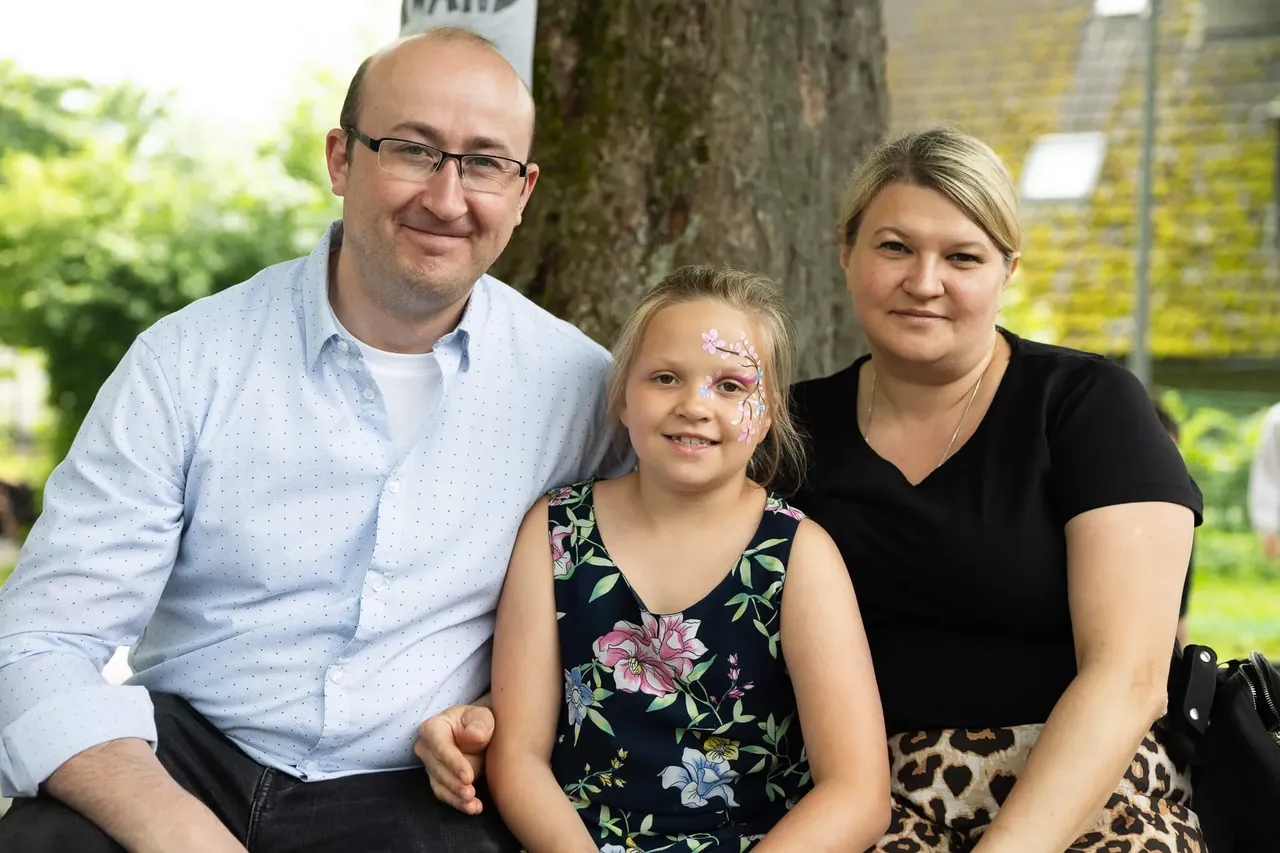Familie mit einem Mädchen im Schulalter, das Gesichtsbemalung trägt, posiert vor Bäumen während des Schulfestes der Humboldtschule.