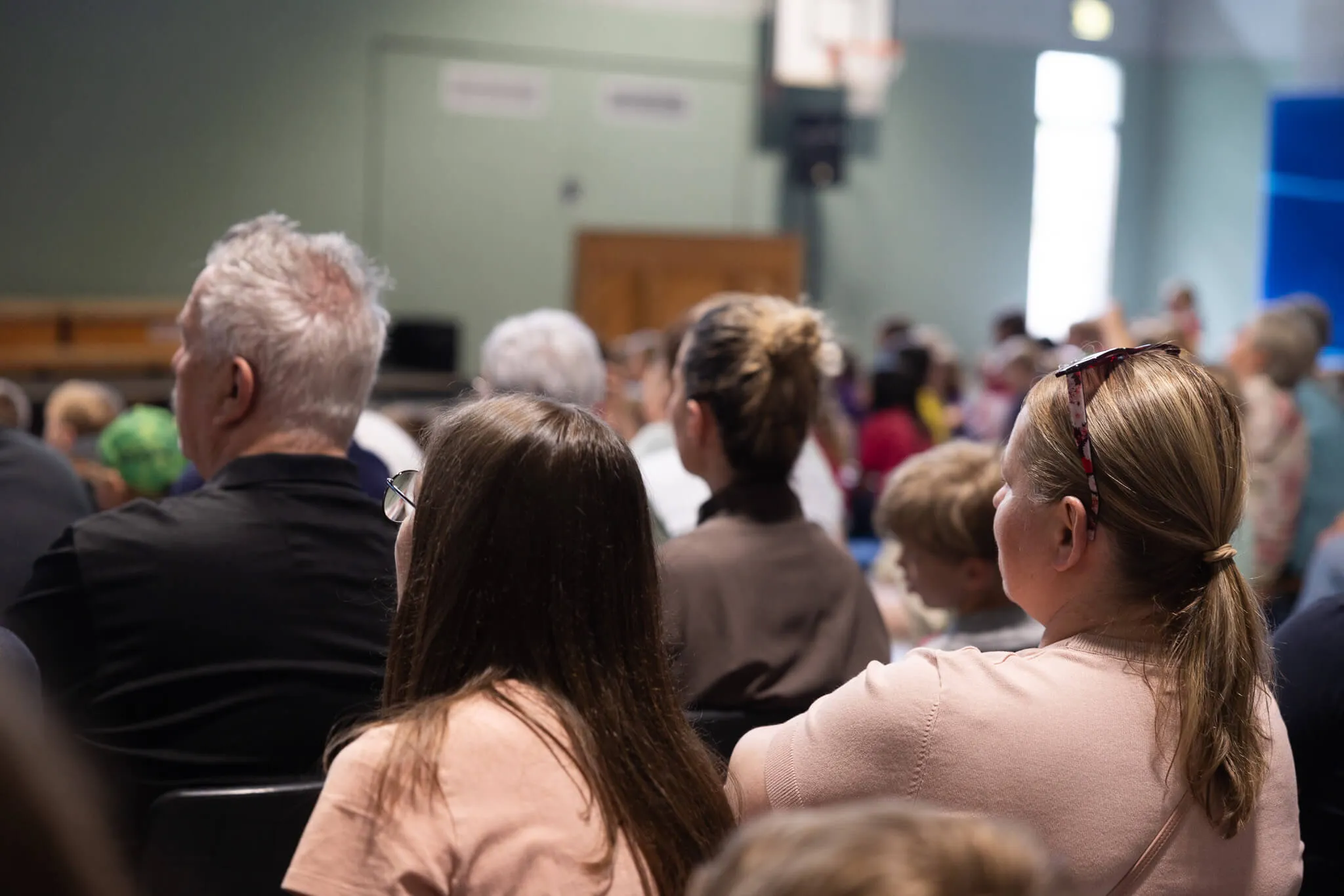 Zuschauer sitzen auf Stühlen in einem Raum und blicken nach vorne, vermutlich während einer Veranstaltung in der Lindenhofschule.