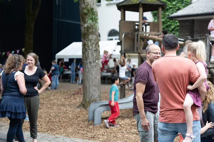 Menschengruppen stehen und unterhalten sich auf dem Gelände der Lindenhofschule, im Hintergrund ein Spielplatz und ein Zelt.