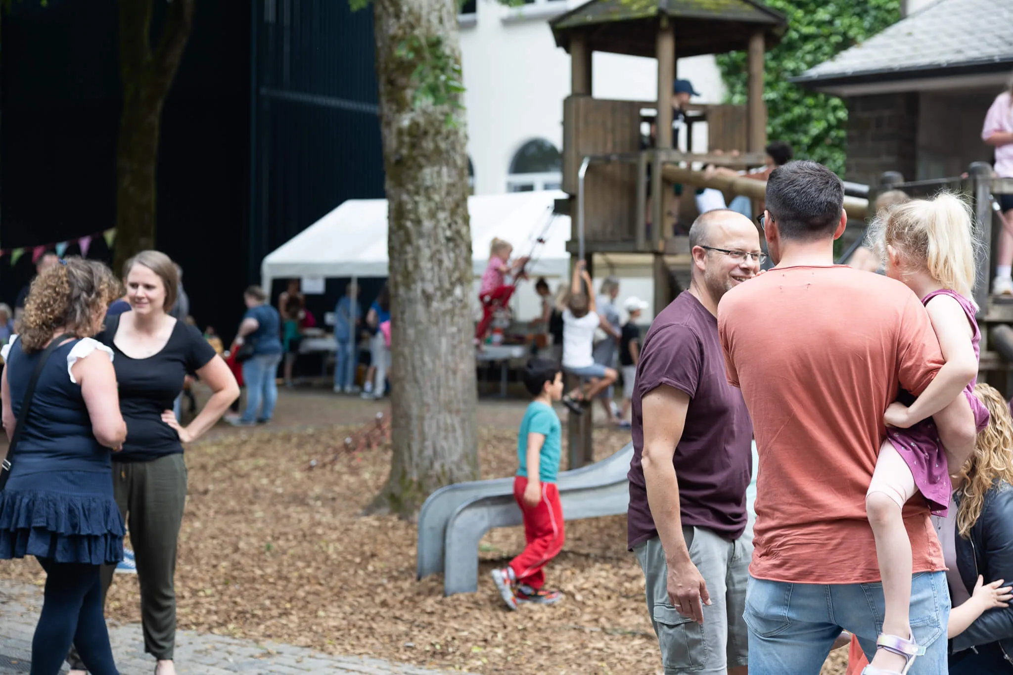 Menschengruppen stehen und unterhalten sich auf dem Gelände der Lindenhofschule, im Hintergrund ein Spielplatz und ein Zelt.