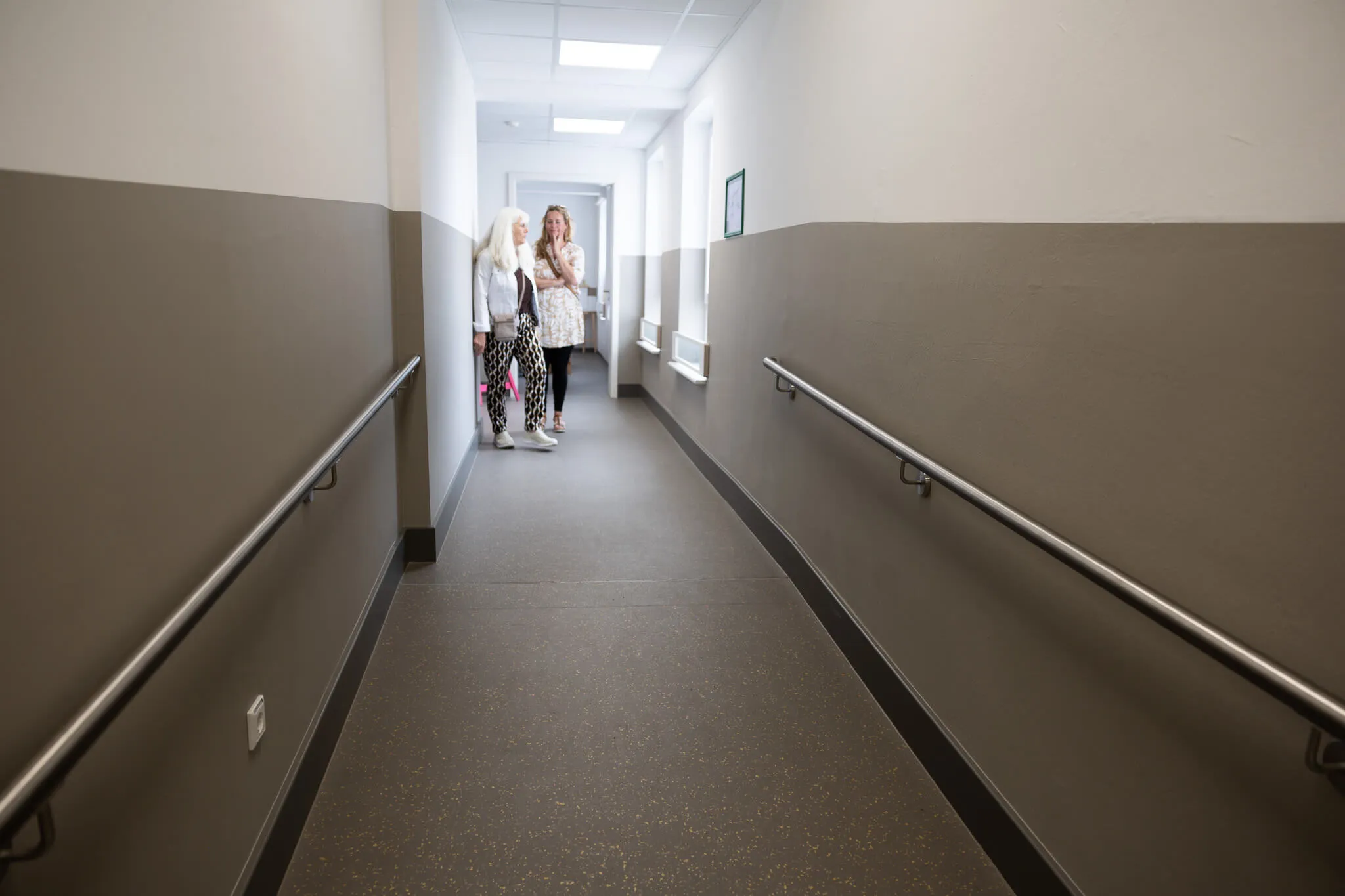 Drei Frauen stehen in einem hellen Flur eines Schulgebäudes und unterhalten sich. An den Wänden befinden sich Handläufe.