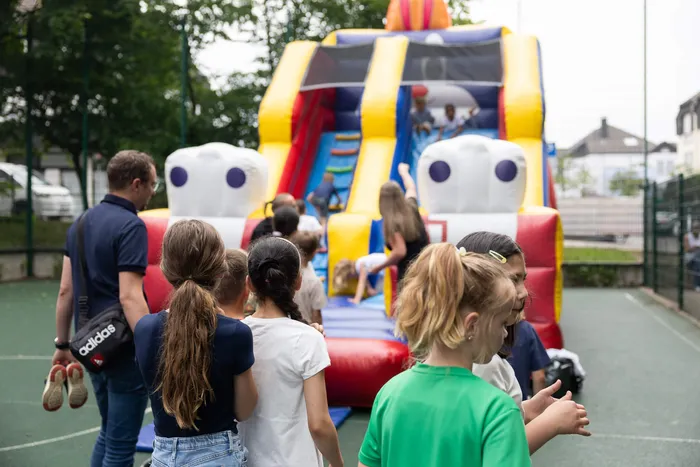Kinder stehen vor einer bunten Hüpfburg und warten auf ihren Zug, während im Hintergrund Erwachsene zusehen.