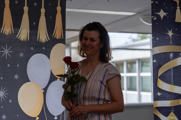 Frau mit roten Rosen lächelt in die Kamera, umgeben von Luftballons und dekorativen Säulen mit Fransen und Sternenmotiven. Sie gehört zu den Absolventen der Höheren Handelsschule, die von der ESBK verabschiedet werden.