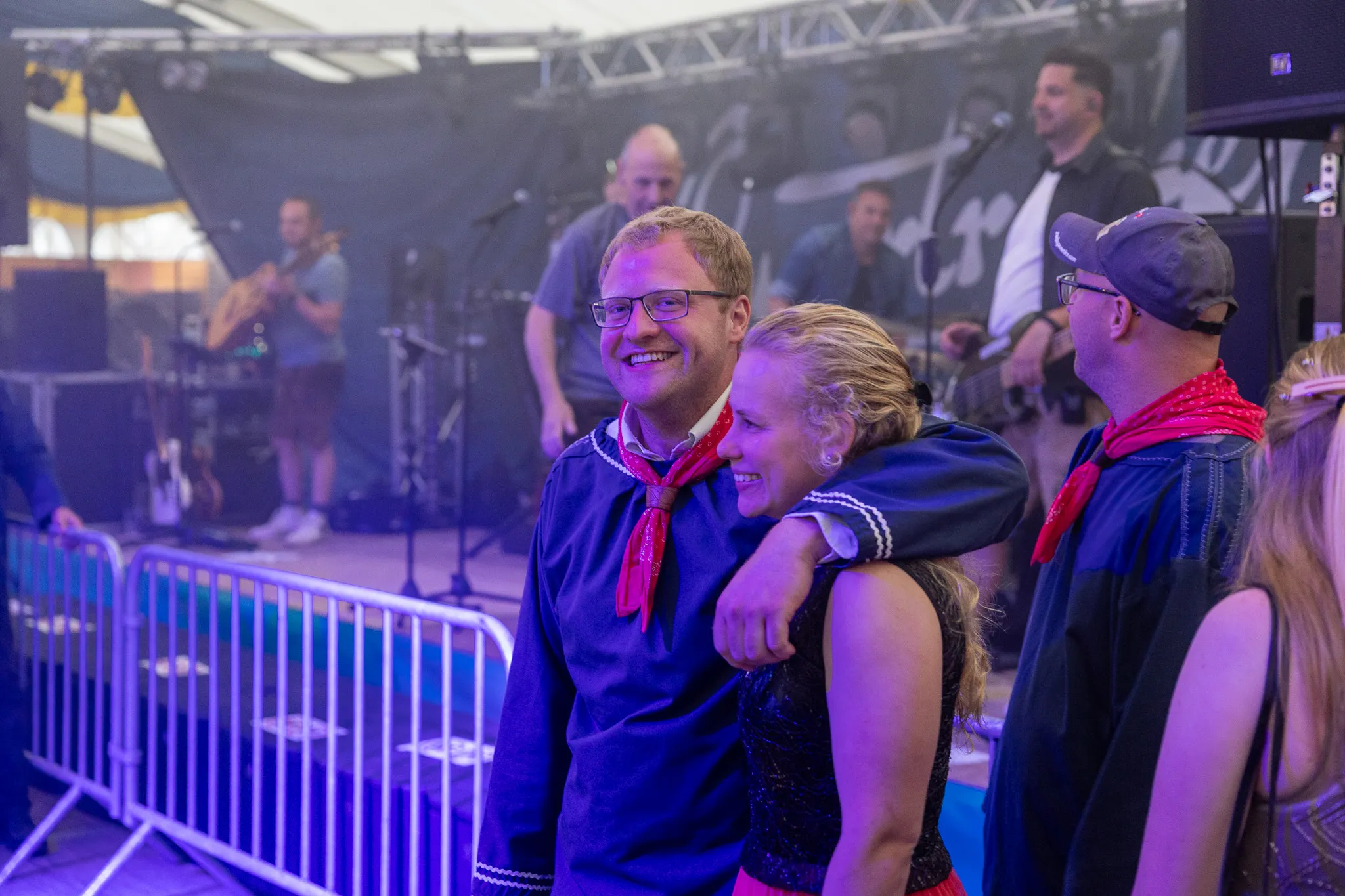 Ein lächelnder Mann mit Brille wird von einer Frau umarmt, während im Hintergrund eine Band auf einer Bühne spielt. Das Festzelt ist mit Besuchern gefüllt.