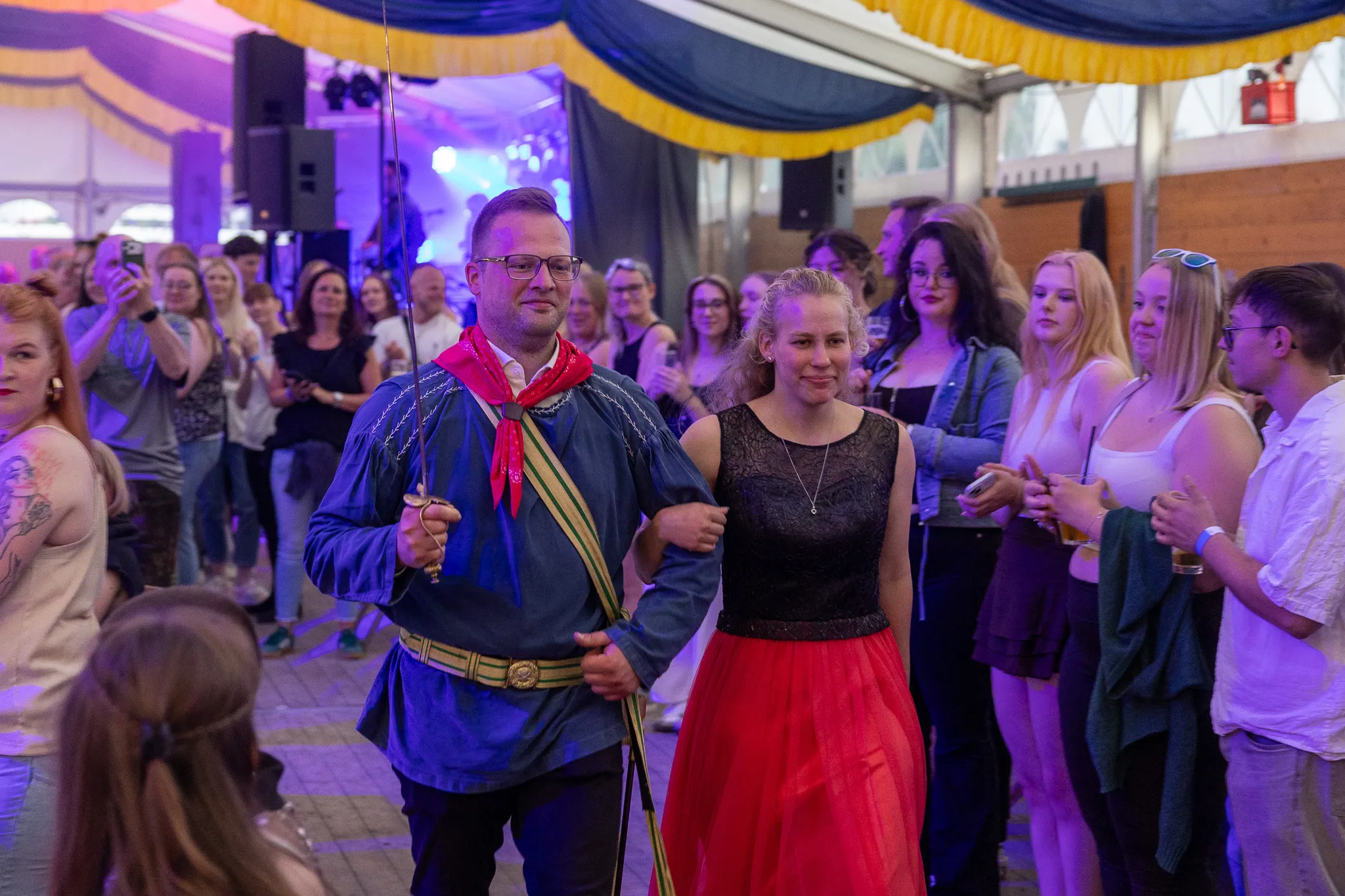 Ein Mann und eine Frau in traditioneller Tracht tanzen im Festzelt, umgeben von zuschauenden Menschen.